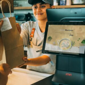 A smiling cashier hands a paper bag to a customer at a modern point of sale, showcasing customer service.