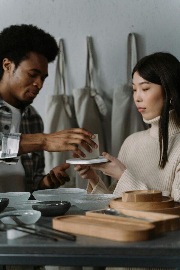 An African American man and Asian woman interact in a store with dishware and tableware on display.